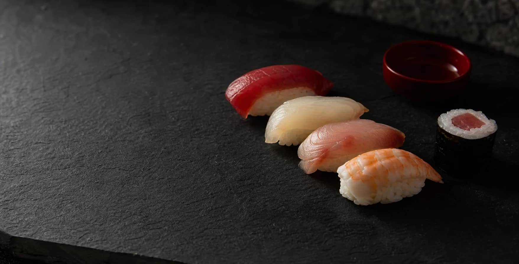 Imagem conceitual de peças de sushi organizadas com espaço negativo sobre uma superfície escura.
